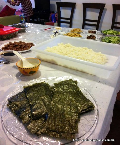 Mesa com arroz de sushi e ingredientes do recheio para o temaki. Alga nori em primeiro plano.