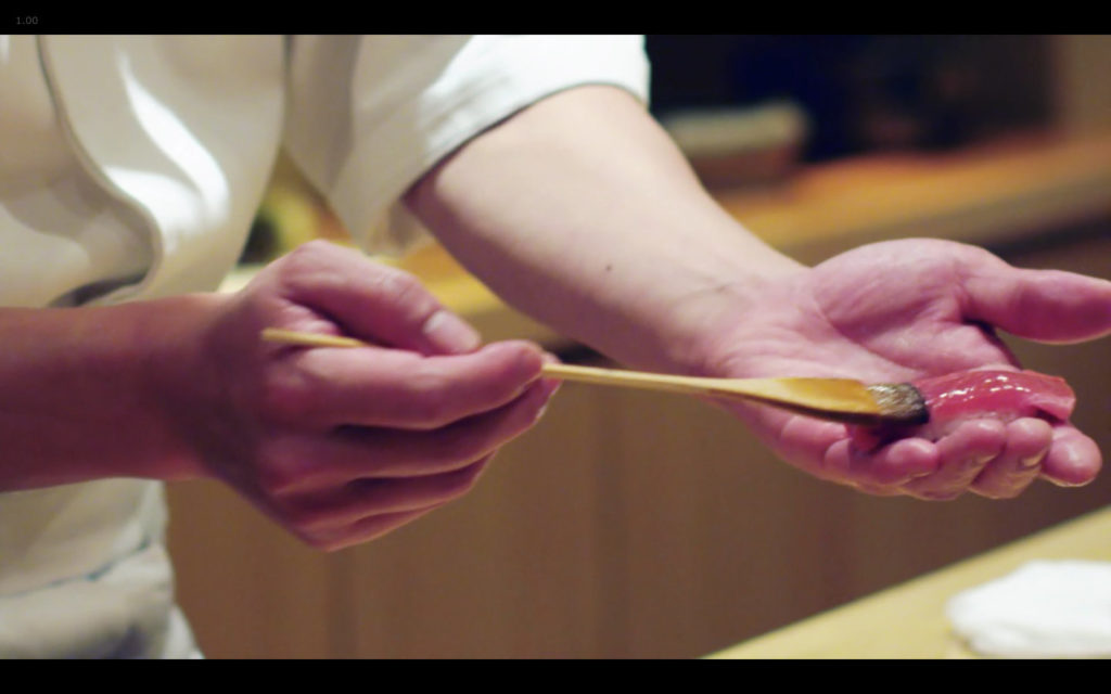 Cena de Jiro Dreams of Sushi: chef passando (pouco) shoyu no sushi com pincel